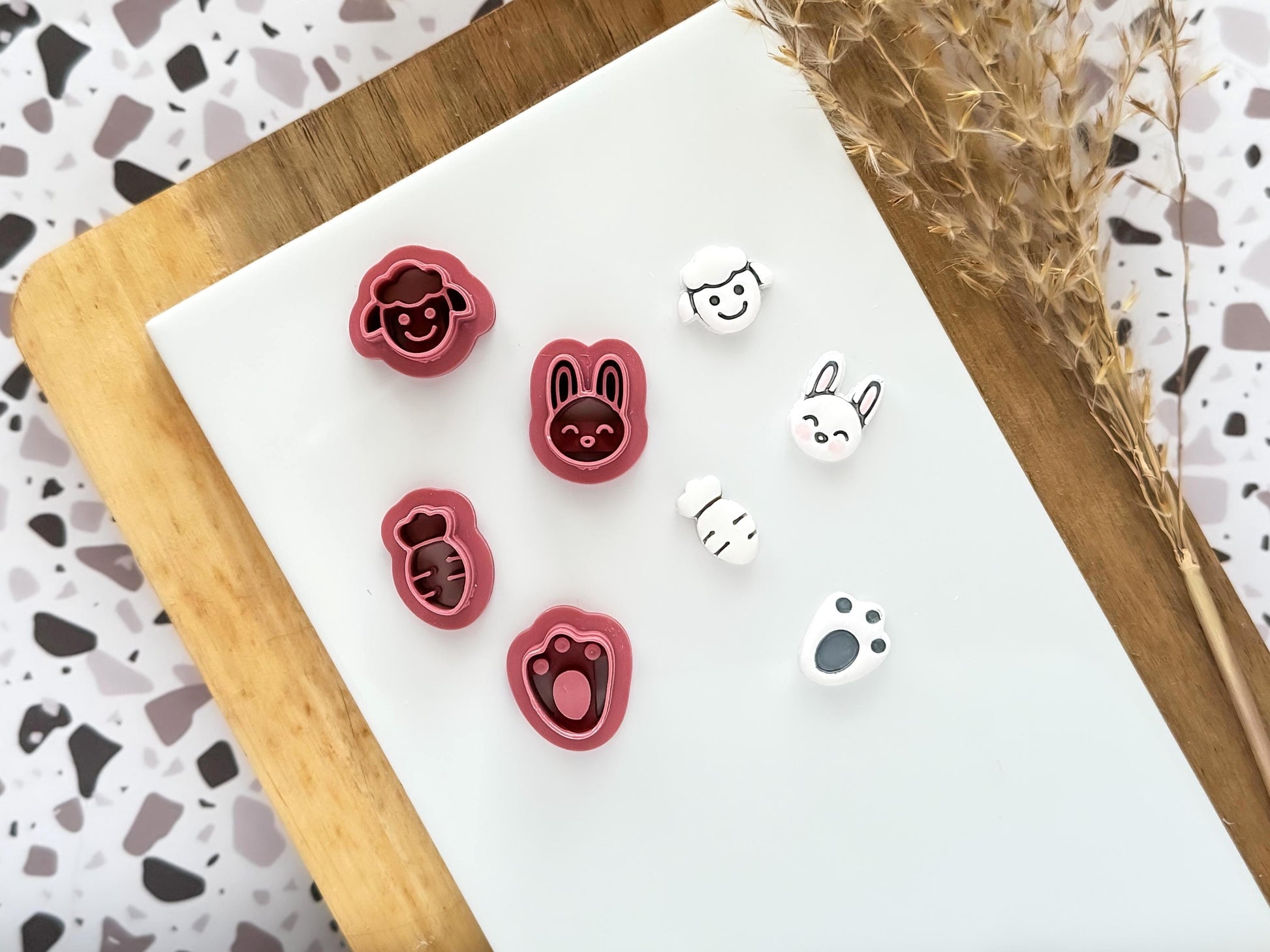 Set of 4 miniature Easter themed clay cutters in the shale of a rabbit face, sheep face, carrot and rabbit's footprint all 1.5cm in size. Nex to the cutters are 4 polymer clay cut out samples.