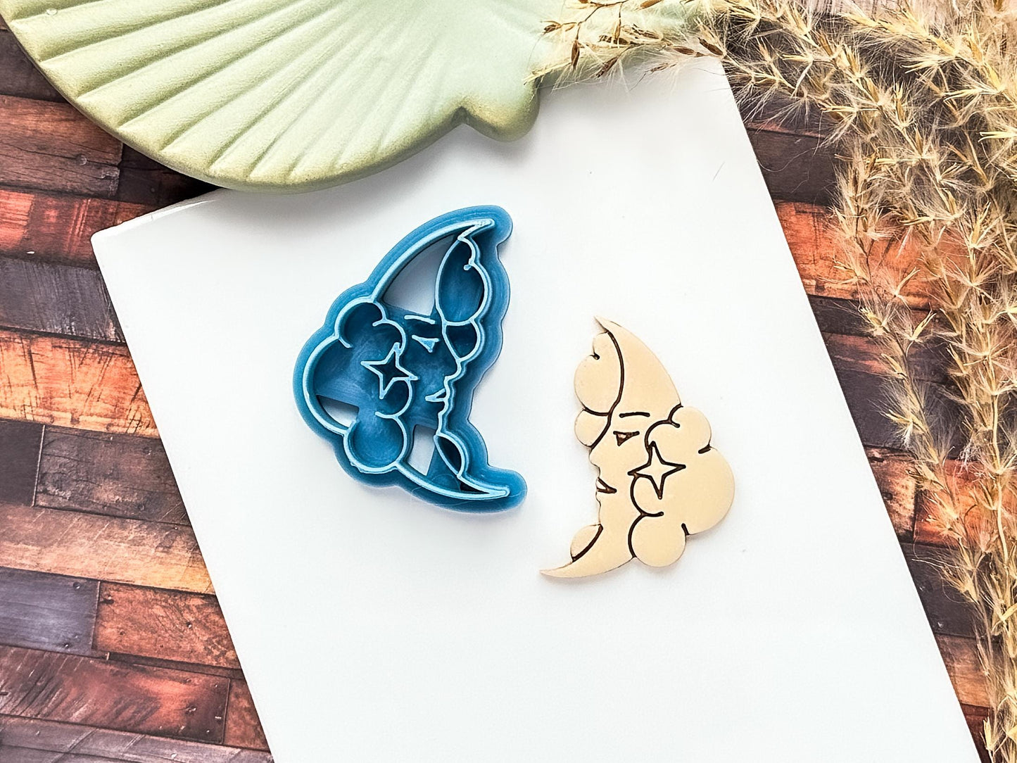 Blue clay cutter in the shape of a crescent moon with fluffy clouds and 4 point star detail. Traditional tattoo style. Next to the cutter is a polymer clay cut out sample.