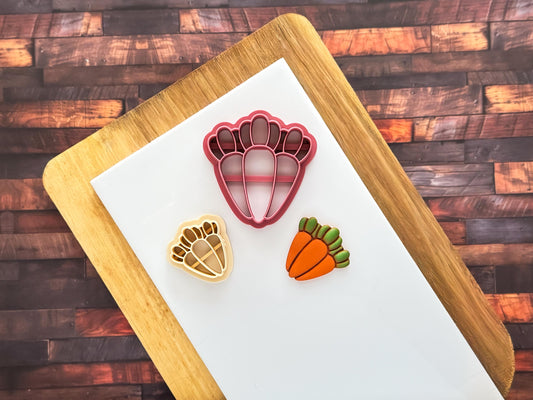 2 sizes of carrot bunch cutter with polymer clay cut out sample that has been painted with liquid clay, all sat on a white baking tile