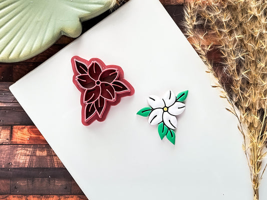 pink jasmin flower polymer clay cutter with pointed petals and leaves alongside a clay cut out sample on a white baking tile.