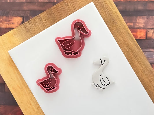 Small and large duck shaped clay cutters next to a grey polymer clay cut out and painted sample.