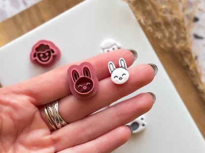 mini rabbit face clay cutter and polymer clay cut out in a hand for scale. The cutter and cut out rest on 2 fingers.