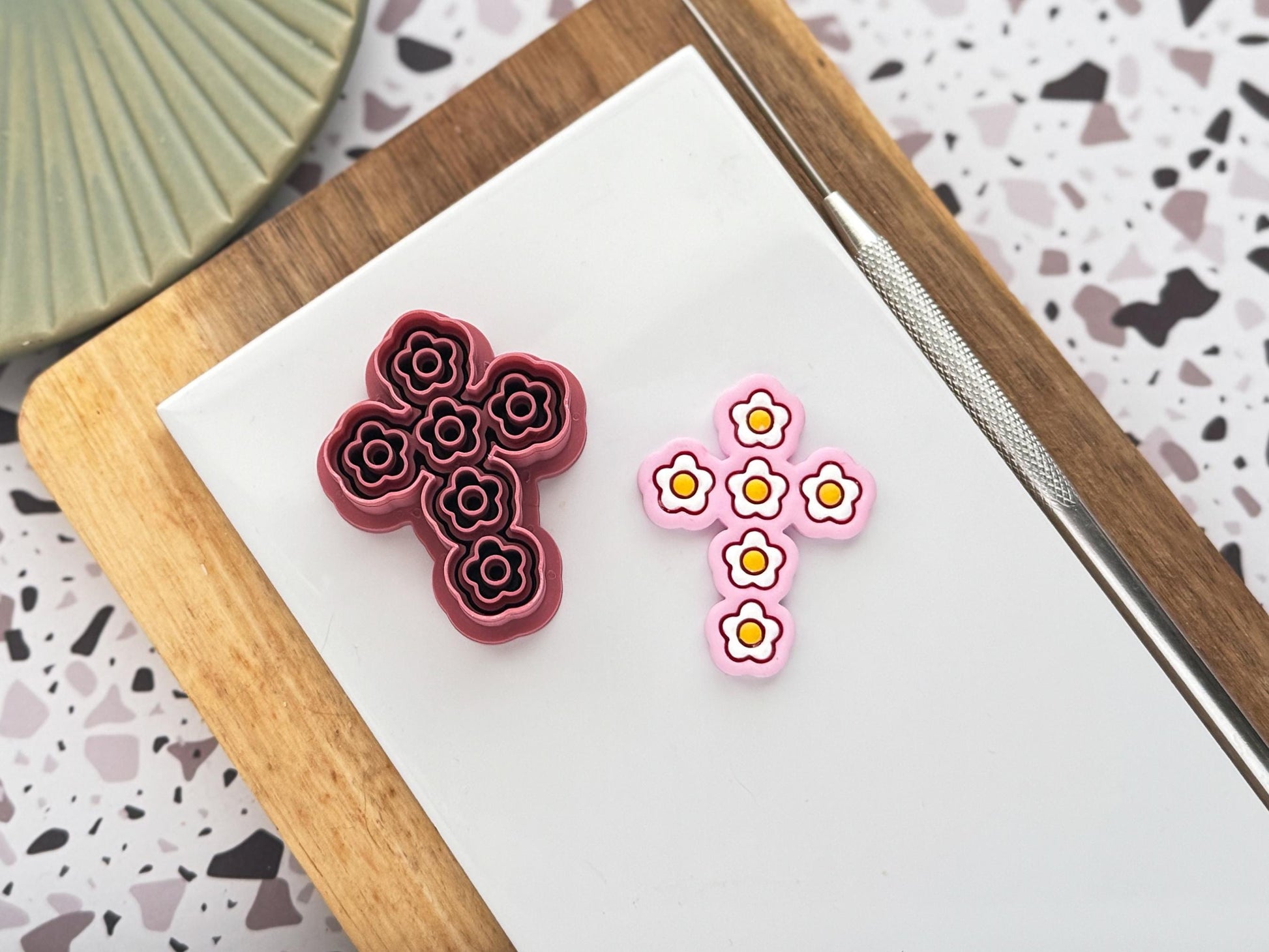 cross shaped clay cutter with daisy stamp details in dar pink with a pastel pink polymer clay cut out earring sample with painted white and yellow daisy flowers