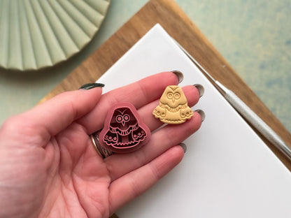 2.5 cm owl clay cutter being held in a hand with a sample polymer clay cut out next to it to show scale.