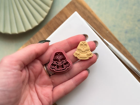 2.5 cm owl clay cutter being held in a hand with a sample polymer clay cut out next to it to show scale.