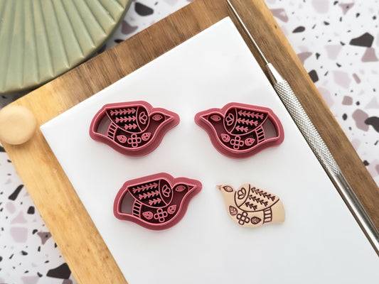 Tribal folk style flying bird cutter for polymer clay and fondant. the images shows a mirrored pair of cutters and a single cutter, as well as a clay sample cut out decorated in a faux ceramic style.