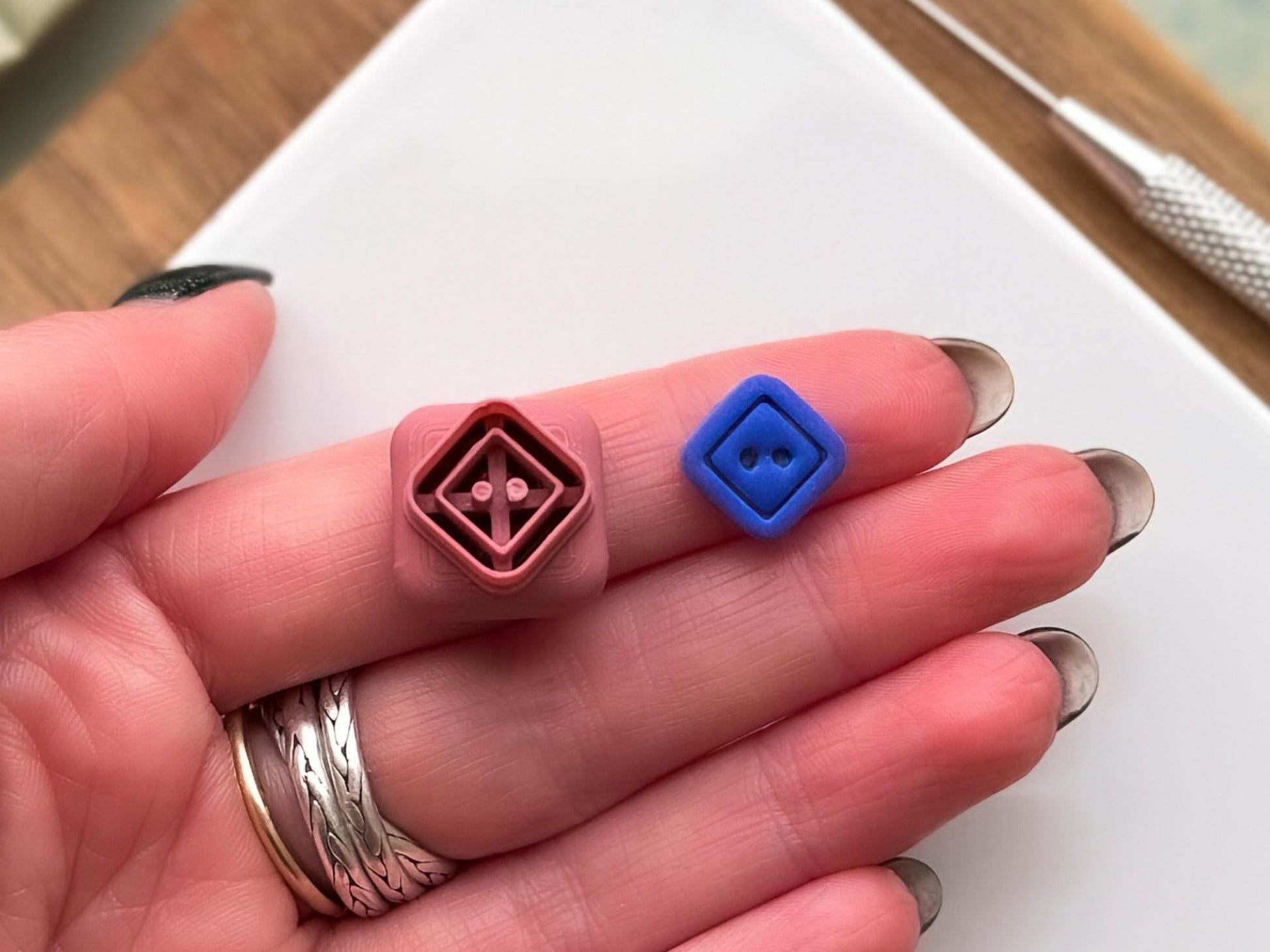 Small diamond shaped button clay cutter and blue clay sample piece in hand for scale