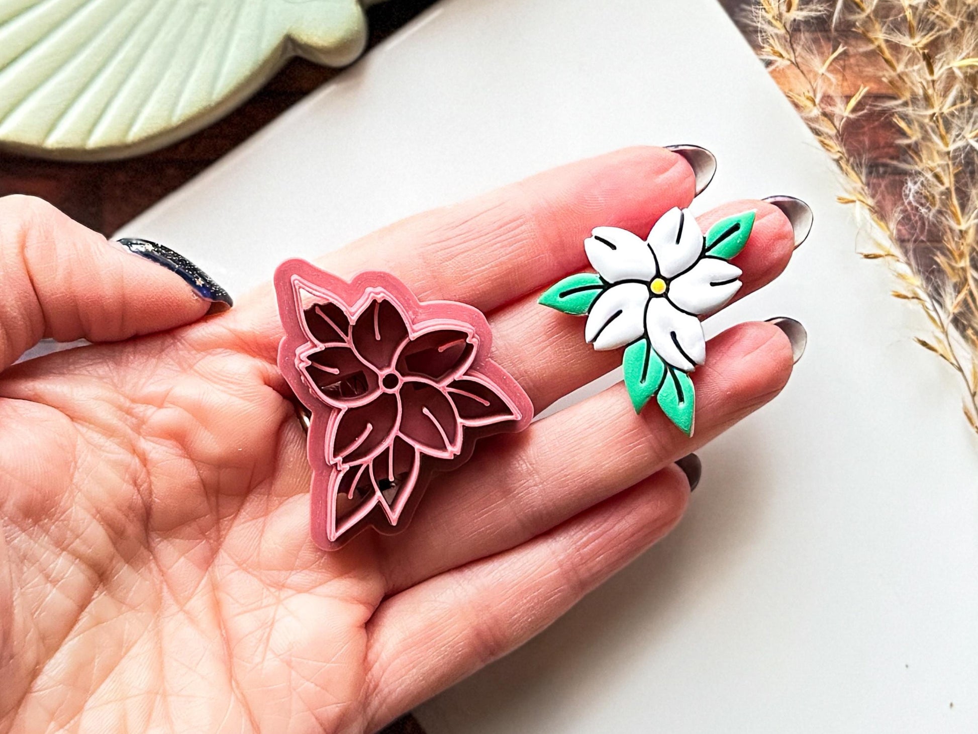 Floral clay cutter in the shape of a jasmin flower and a painted polymer clay cut out sample being held in a hand.