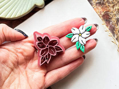 Floral clay cutter in the shape of a jasmin flower and a painted polymer clay cut out sample being held in a hand.