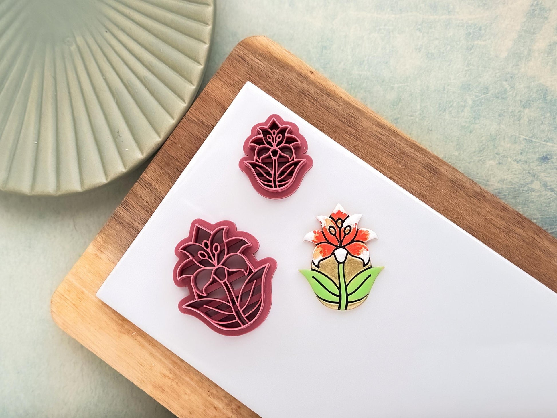 Pink front facing lily cutter in a teardrop shape, small and large sizes shown. Next to the cutters is a polymer clay sample cut out.