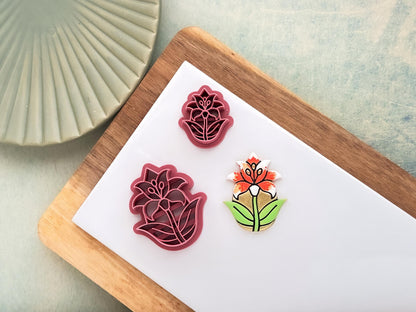 Pink front facing lily cutter in a teardrop shape, small and large sizes shown. Next to the cutters is a polymer clay sample cut out.