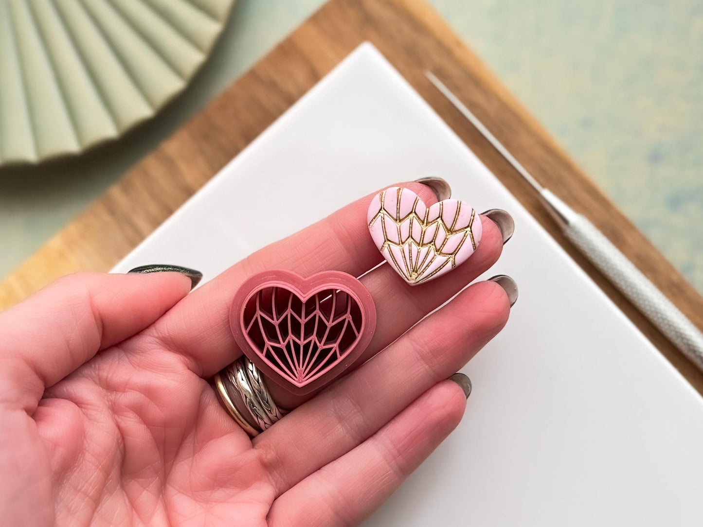 Geometric heart clay cutter set with intricate line design, alongside finished polymer clay heart with gold detailing