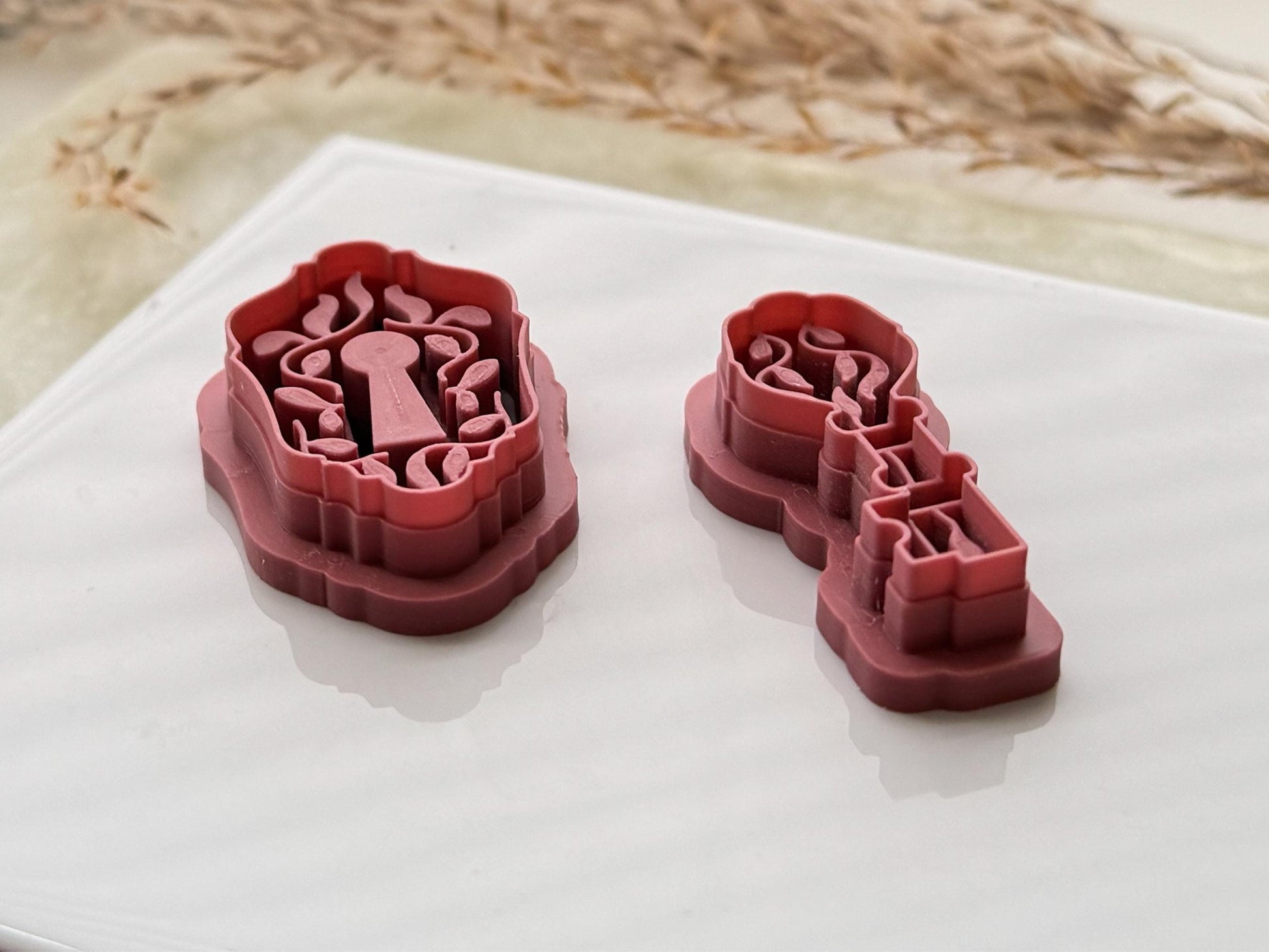 Side view of a lock shaped clay cutter and a key shaped clay cutter in pink, the leaf stamp details can be seen.