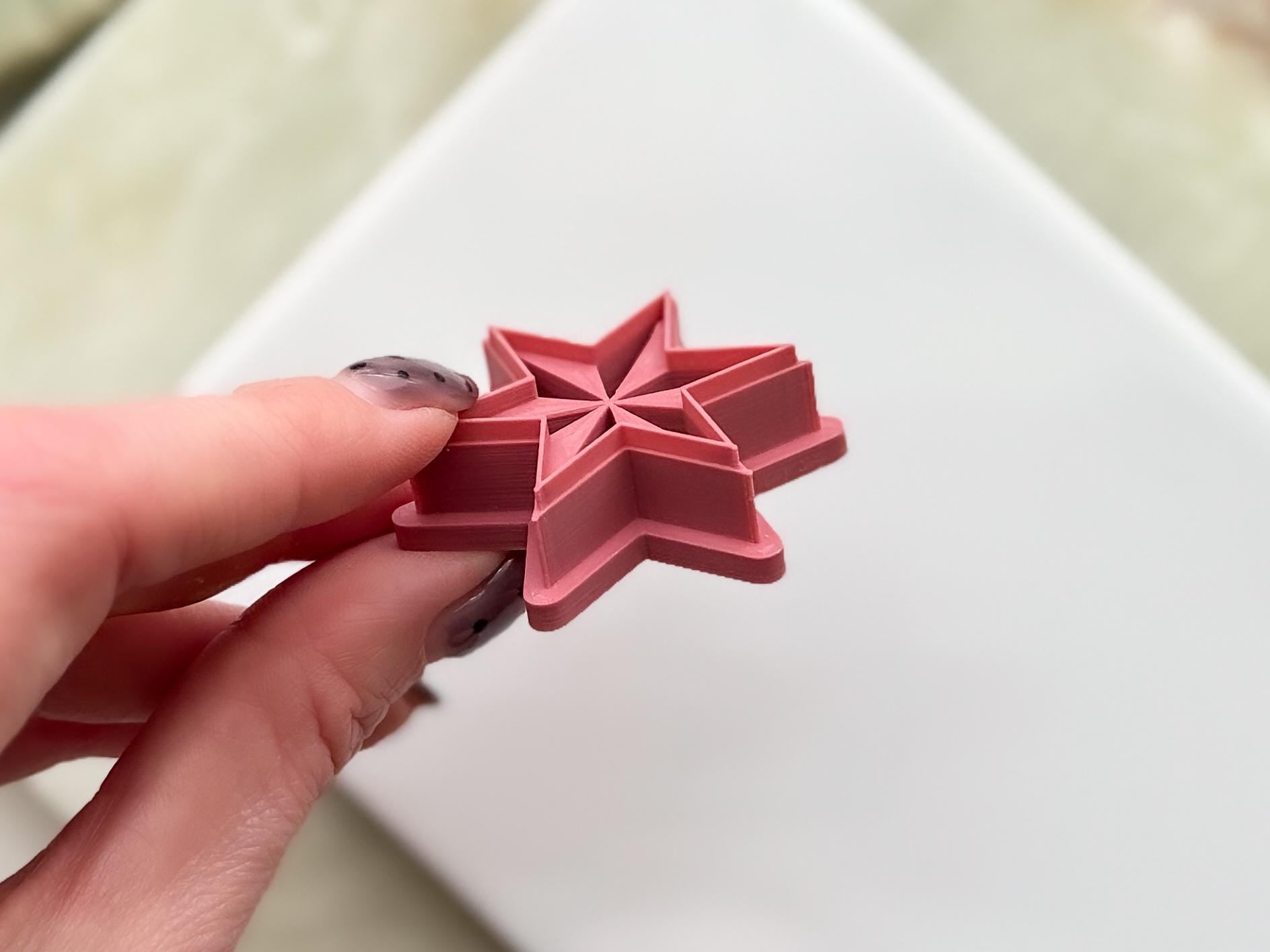 Side view of six point star clay cutters in emo witchy style with debossed sections being held in a hand.