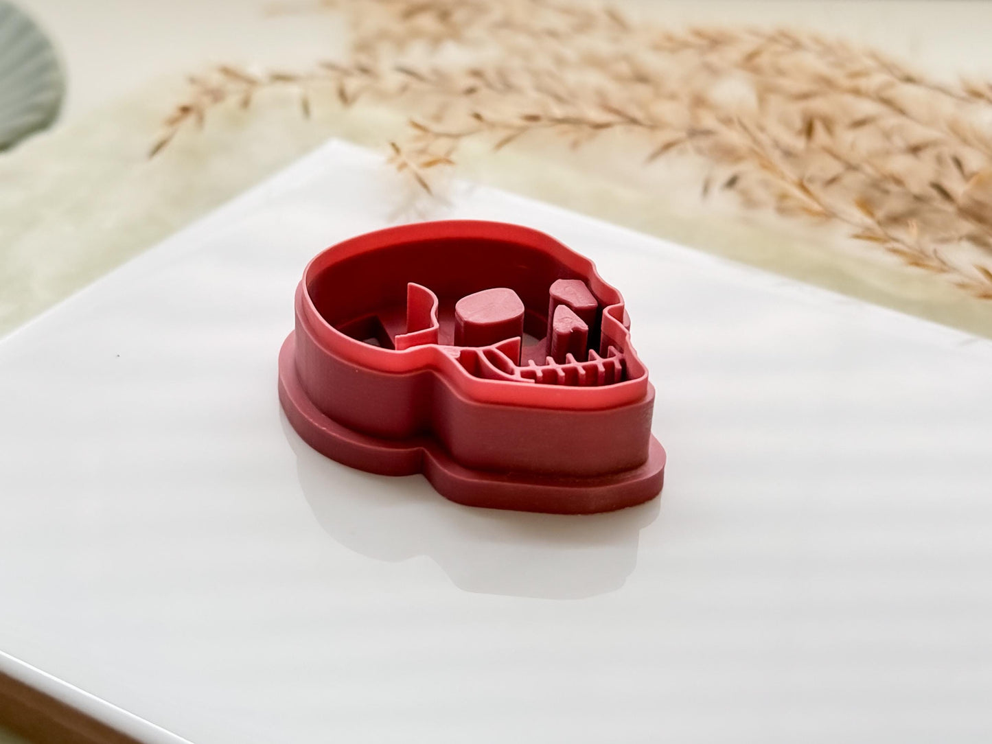 Side view of a skull shaped polymer clay cutter in pink on a white tile