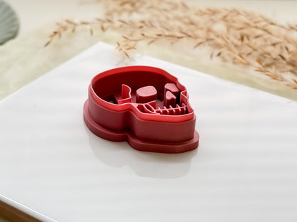Side view of a skull shaped polymer clay cutter in pink on a white tile