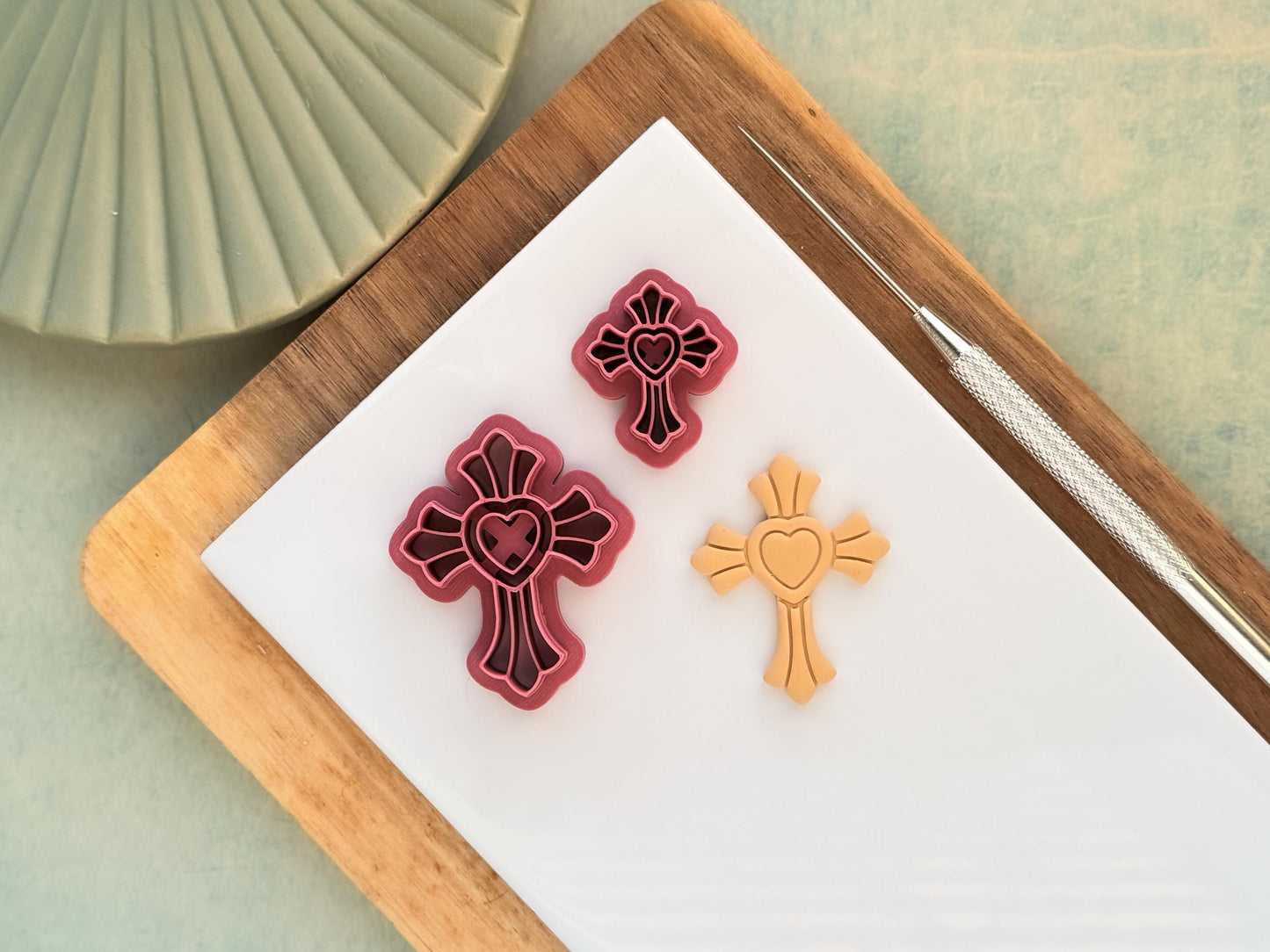 Detailed cross clay cutters in small and large with heart imprint centre. the cutters are a dark pink colour and next to them is a polymer clay cut out sample showing the embossed stamp details.
