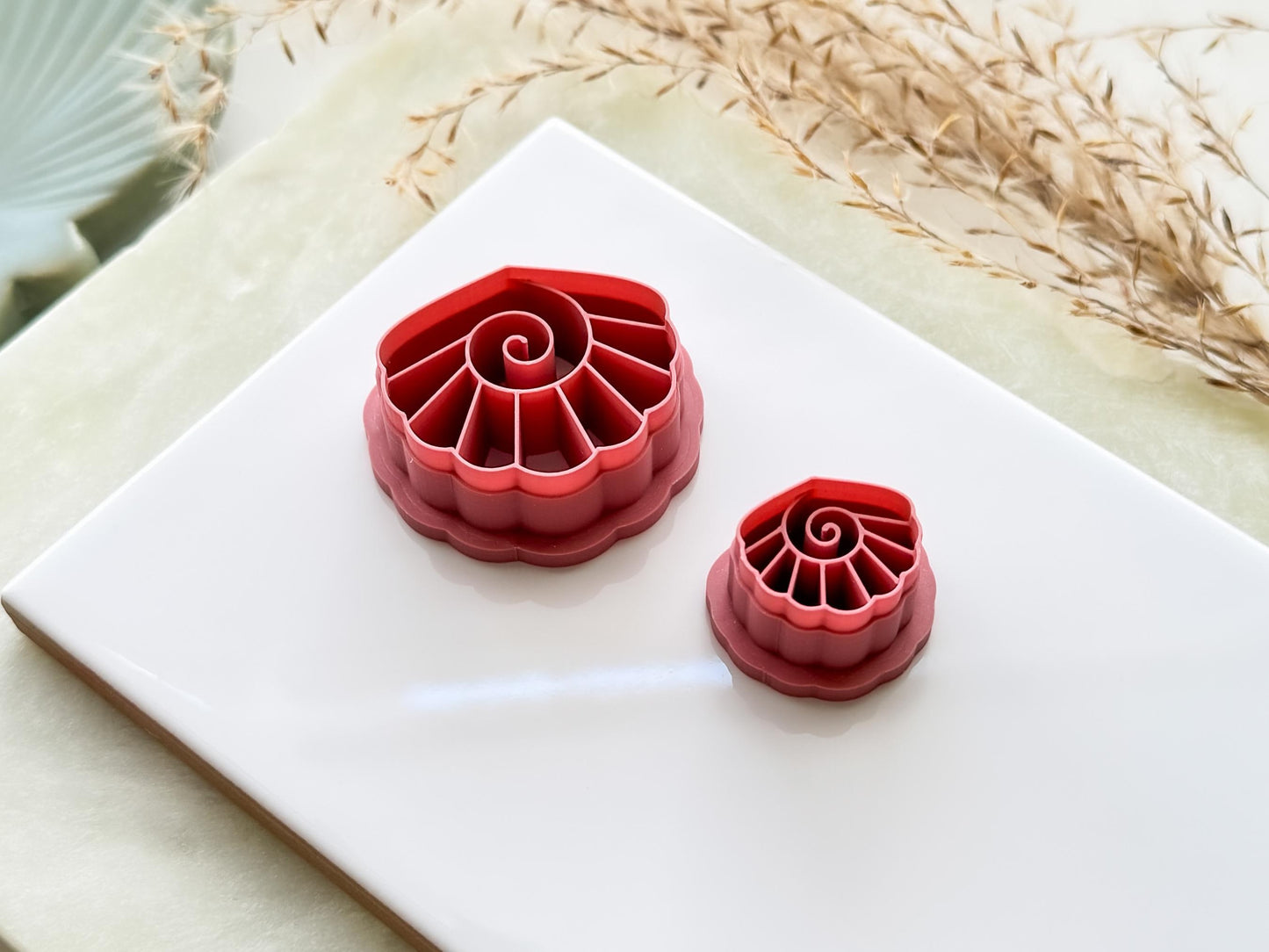 Two scalloped edge shell cutters for use on polymer clay and fondant. The shells have vertical lines and a swirl in the middle.