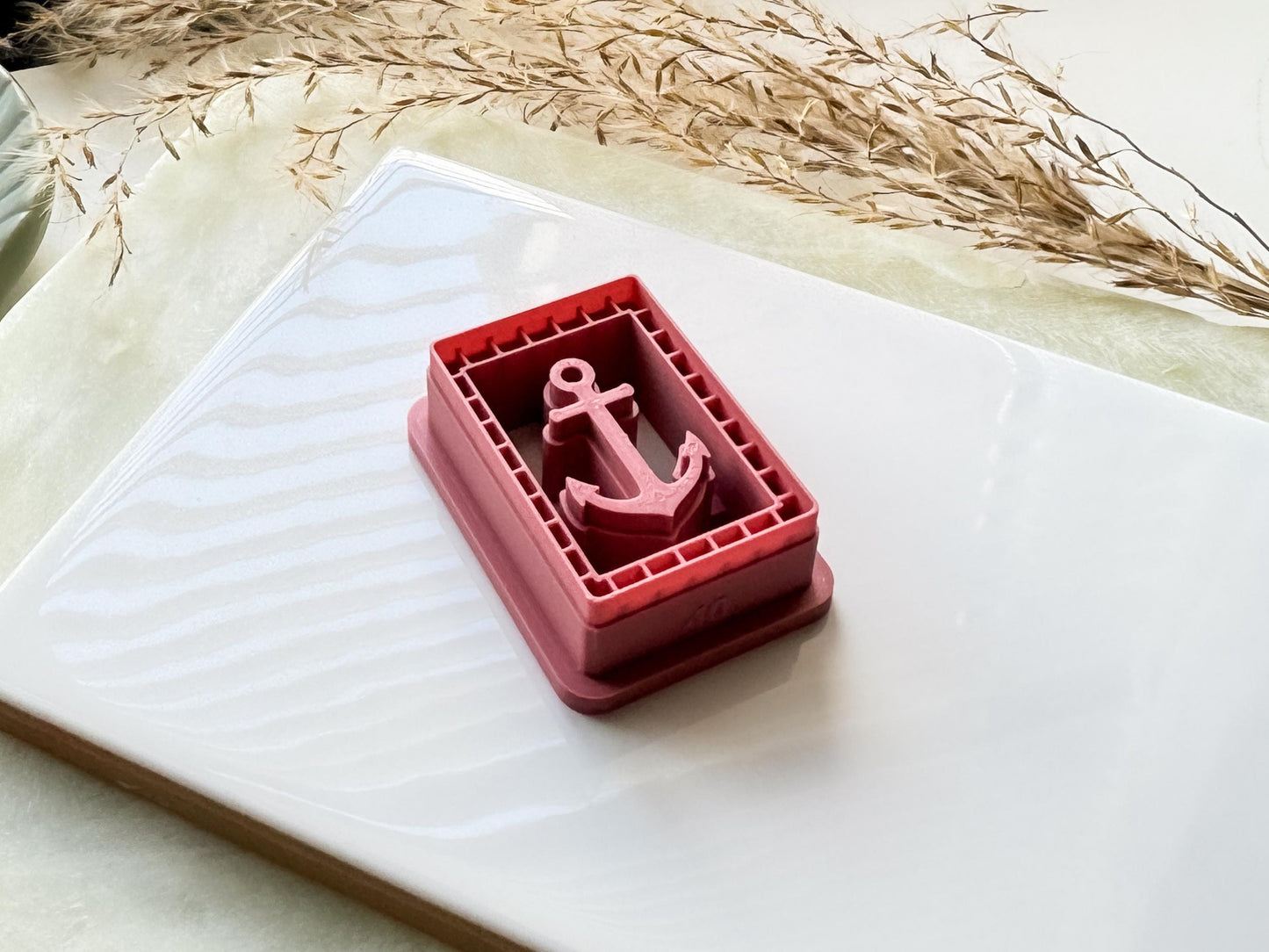 Side view of ocean themed clay cutter with anchor shaped stamp within a frame.