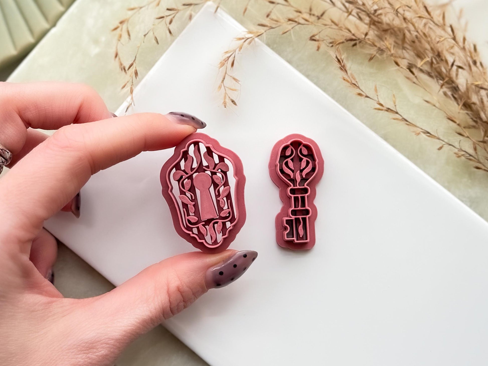 Close up of floral lock clay cutter being held in a hand to show the stamp details and open back for air flow