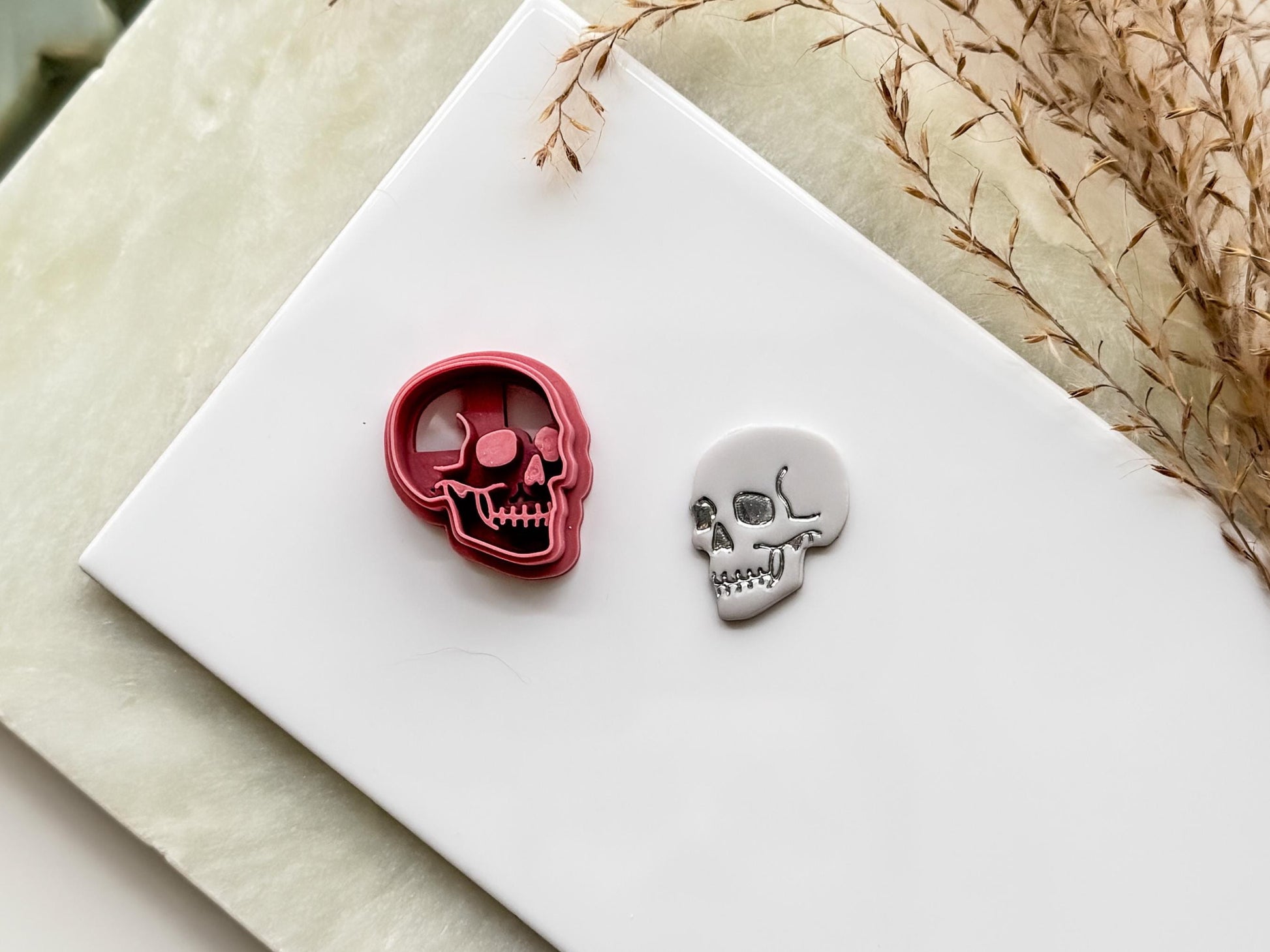 Skull shaped clay cutter side profile detail with eye, nose and mouth details. Next to the cutter is a polymer clay cut out.