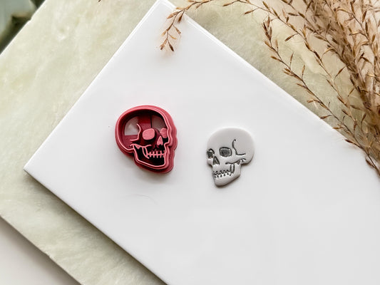 Skull shaped clay cutter side profile detail with eye, nose and mouth details. Next to the cutter is a polymer clay cut out.