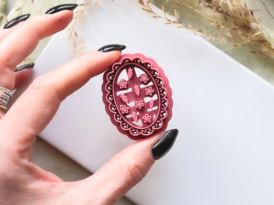 Close up of wavy oval frame cutter with tiny strawberry and flower stamp details for summer themed polymer clay earring making.