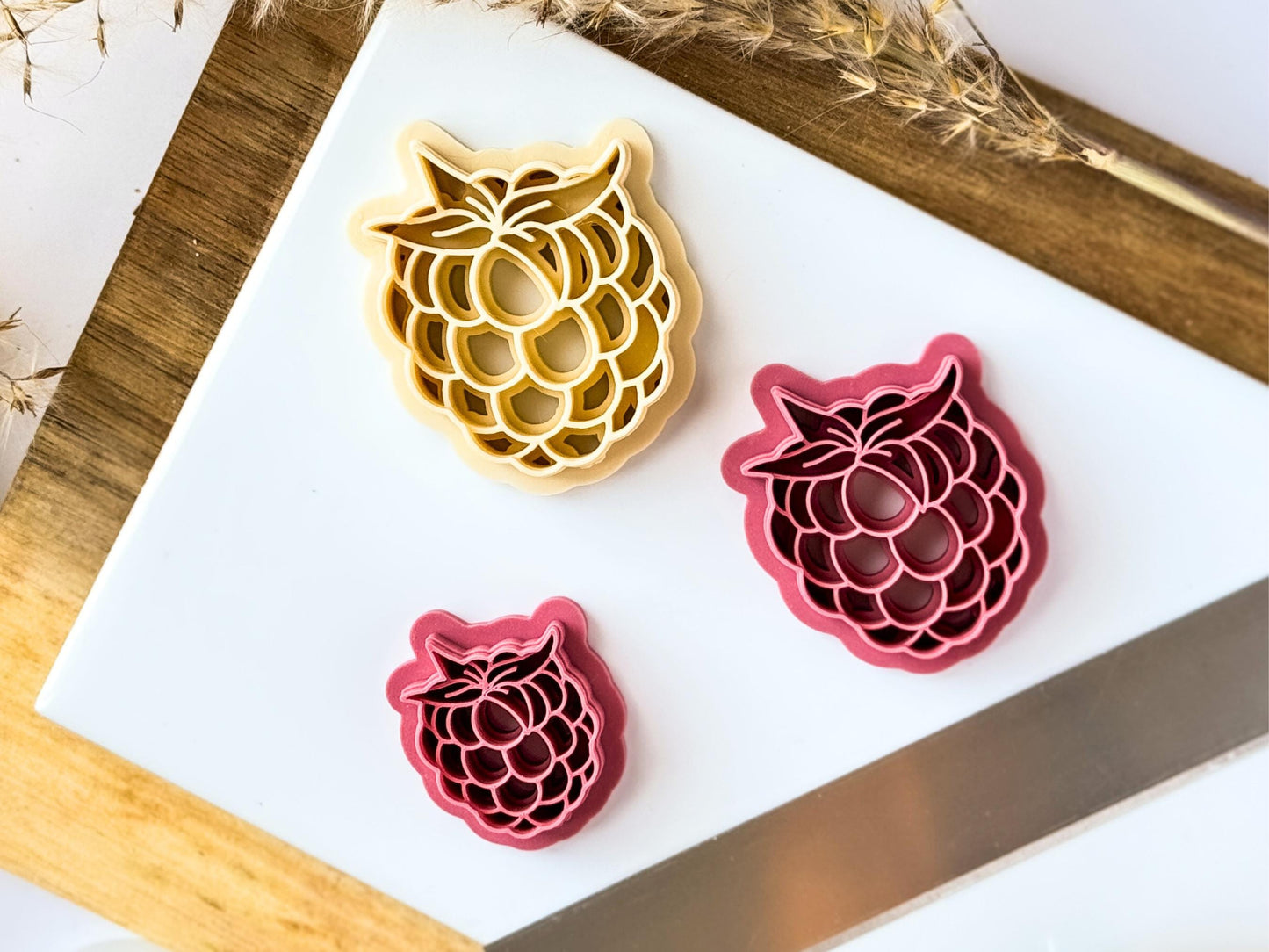 Raspberry shaped clay cutter in different sizes and colours on a white baking tile.