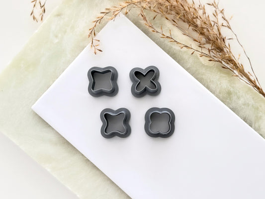 Four small cross shaped clay cutters in a light gray material, they consist of an outline shape only. All polymer clay cutters are on a white tile.