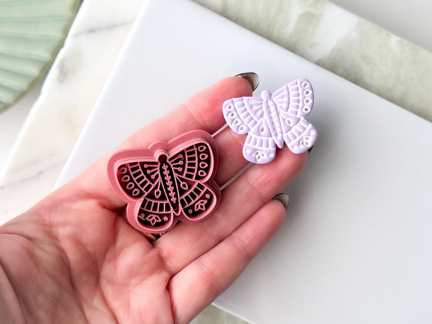 Folk Style Butterfly Cutter in dark pink with a purple clay cut out sample next to it. Both are being held in a hand.