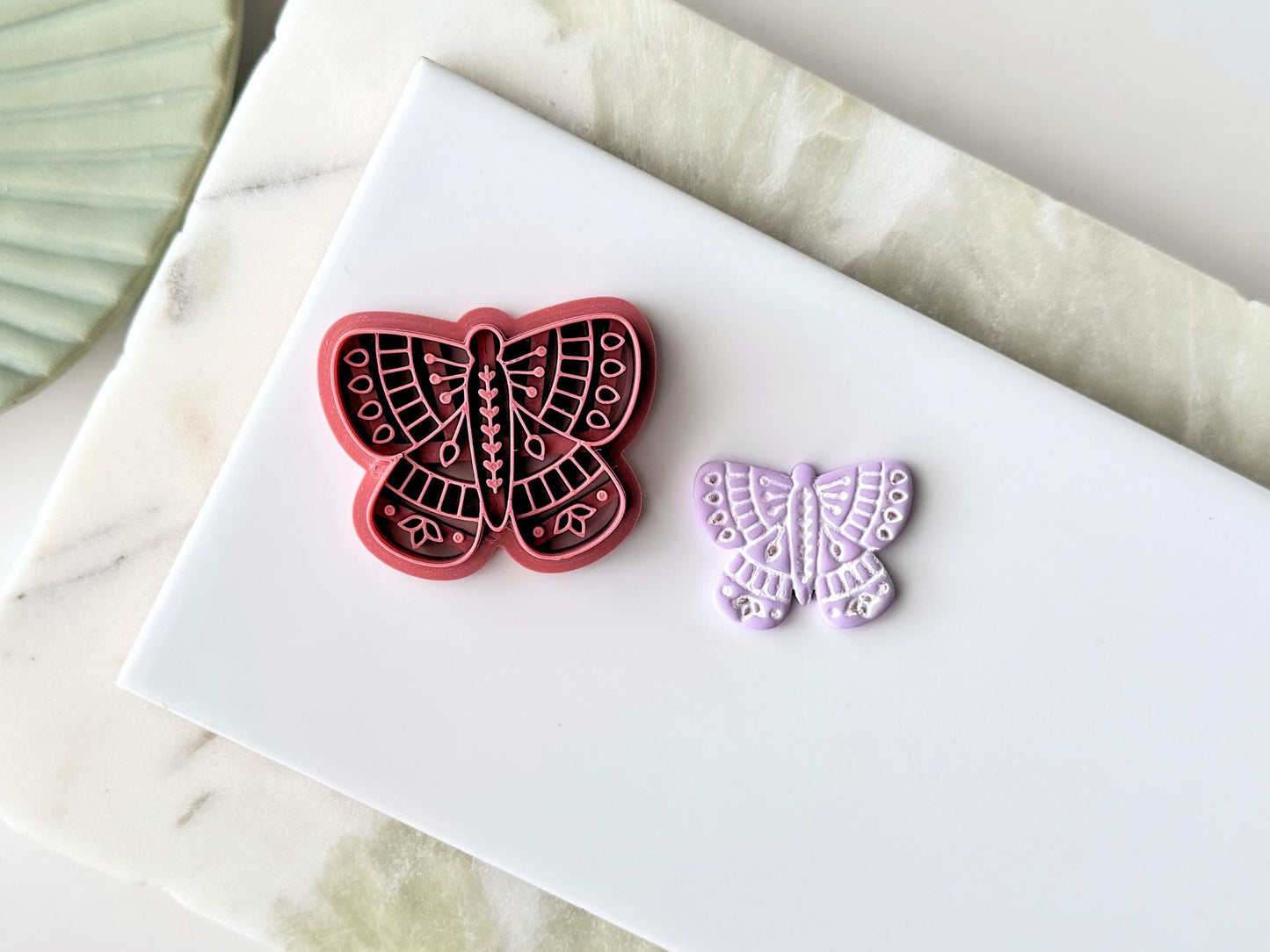 Folk art patterned butterfly clay cutters, nordic floral style imprint patterns. This image features a single large cutter and a purple sample cut out on a white tile.