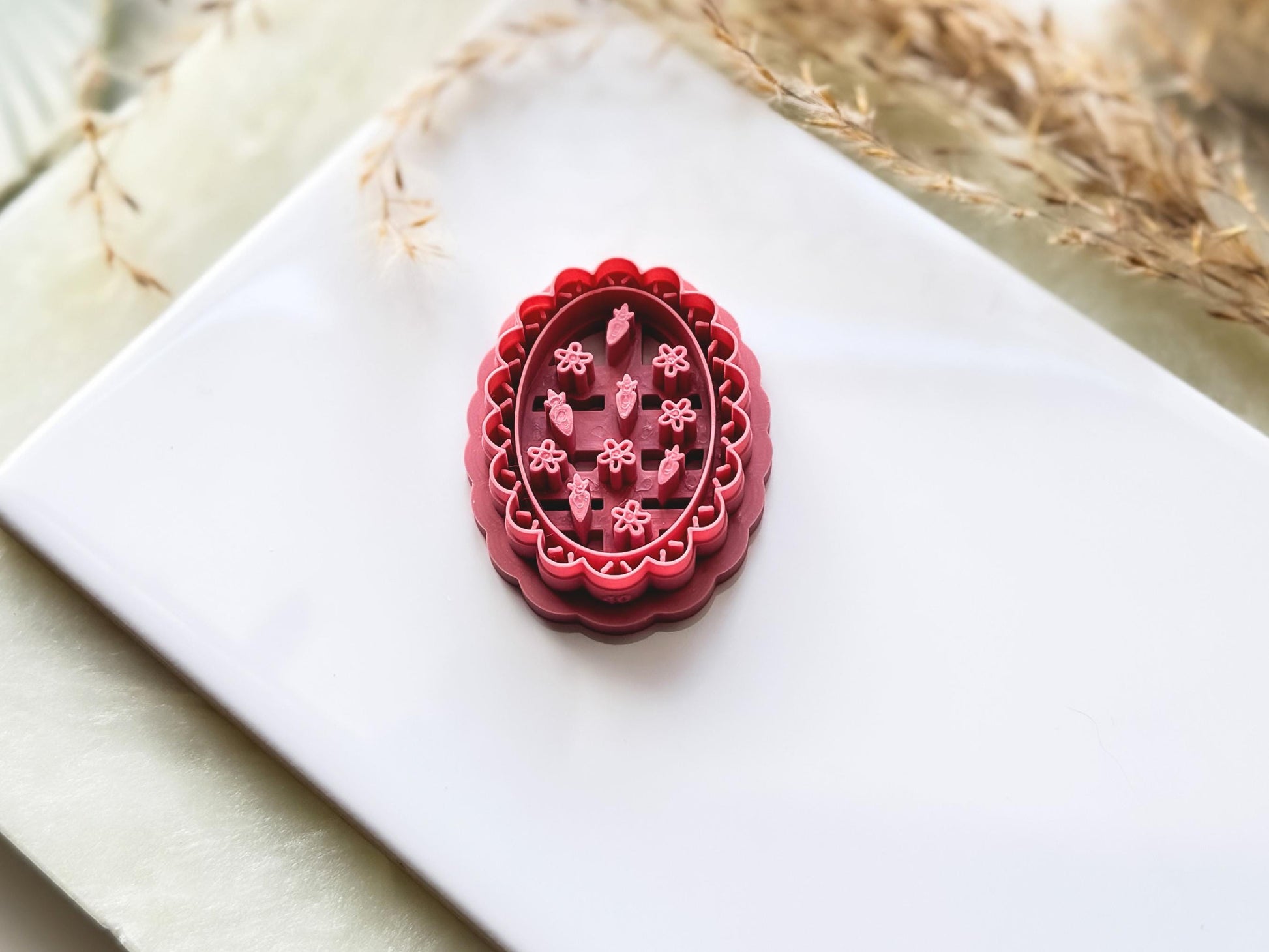 Tilted view of wavy oval frame cutter with tiny strawberry and flower stamp details for summer themed polymer clay earring making.