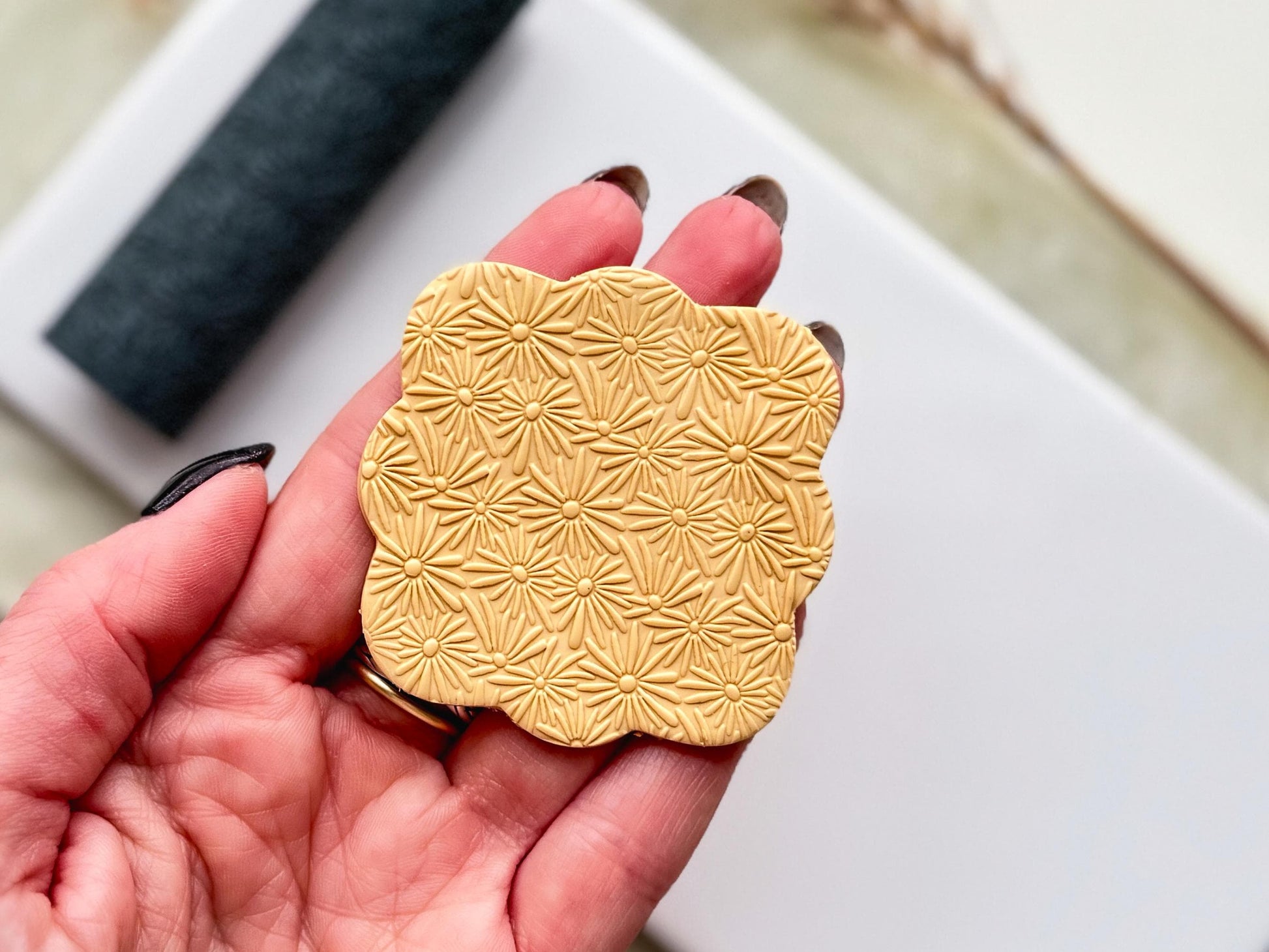 polymer clay cut out with daisy flower pattern being held in a hand