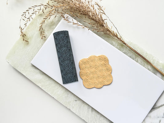 A texturising tool for use on clay, it features a seamless thin petal daisy flower pattern. Next to the clay tool is a square polymer clay cut out with the floral embossed pattern.