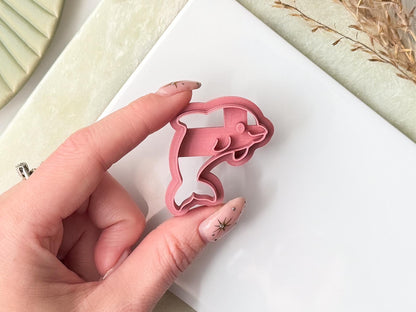 Pink 3d printed clay cutter in the shape of a cute cartoon dolphin being held in a hand.