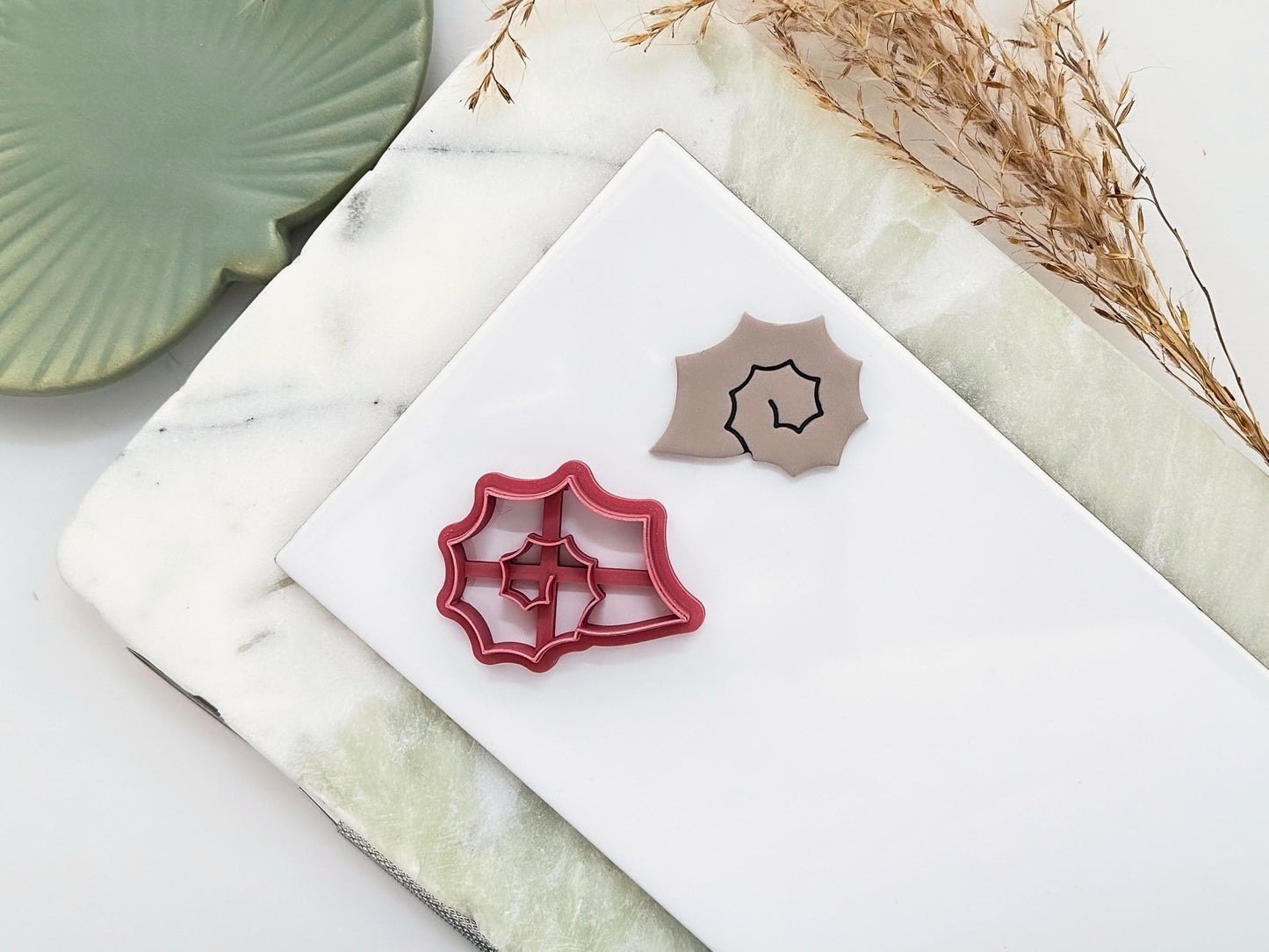 Pink clay cutter in the shape of a spiky sea snail shell featuring a spiral centre. Next to the cutter is a polymer clay sample cut-out of the same shape.