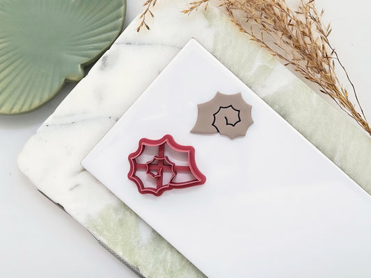 Pink clay cutter in the shape of a spiky sea snail shell featuring a spiral centre. Next to the cutter is a polymer clay sample cut-out of the same shape.
