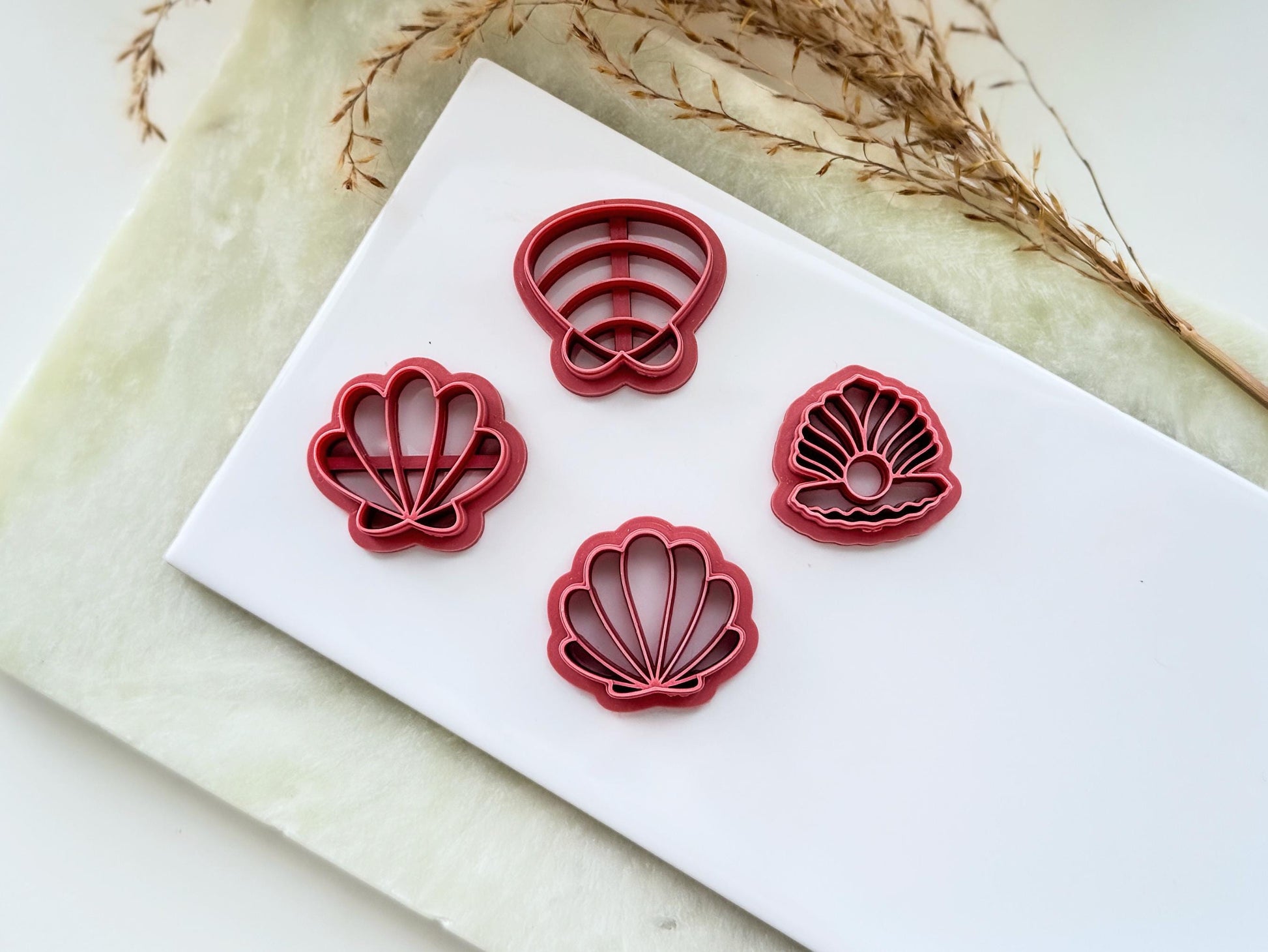 Four shell shaped clay cutters, clamm shells and oyster shell on a white tile.