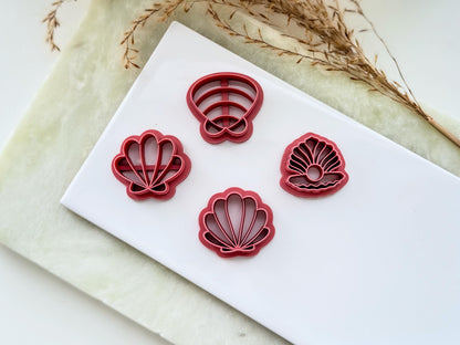 Four shell shaped clay cutters, clamm shells and oyster shell on a white tile.