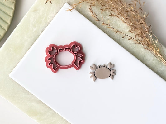 Cartoon style crab clay cutter with pincers, legs and eye details with a polymer clay cut out earring next to it.