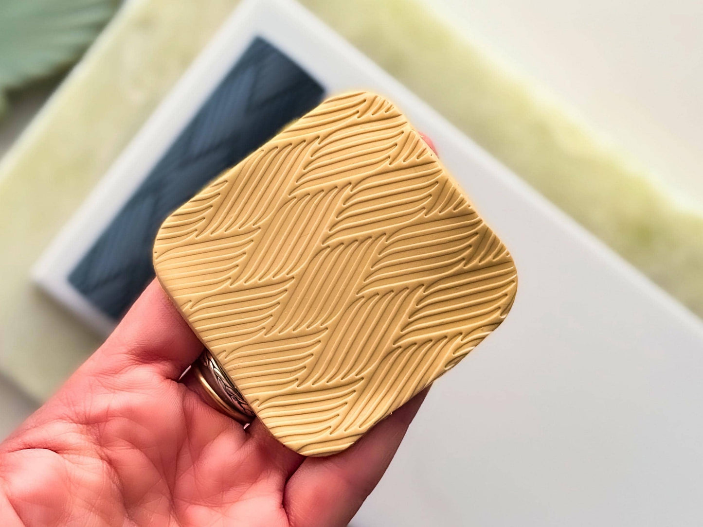Beige polymer clay square ith geometric stripe pattern being held in a hand