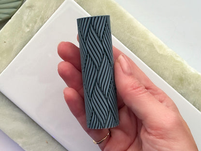 Grey texture roller with wavy line pattern for leaving embossed textures in clay held in a hand.