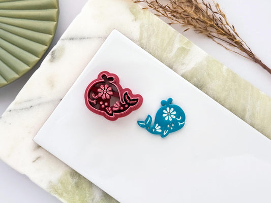 Whale polymer clay cutter with floral embossed design shown alongside matching blue clay cut-out on a white tile. UK-made clay tool for earrings, jewellery, fondant and craft projects.