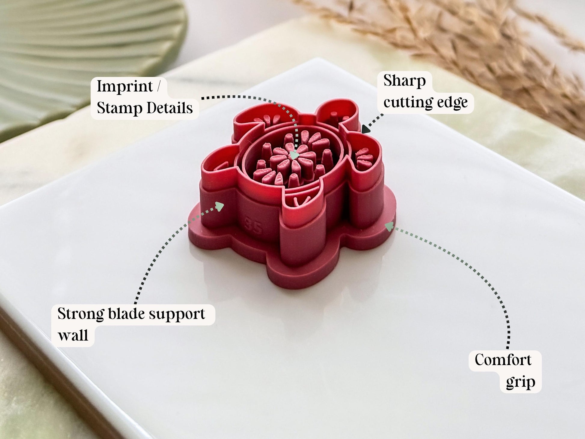 Side view of a sea turtle-shaped polymer clay cutter in dark pink PLA, highlighting the sharp cutting edge, reinforced support wall, embossed stamp details and comfortable grip handle. Displayed on a white tile with decorative dried grasses.