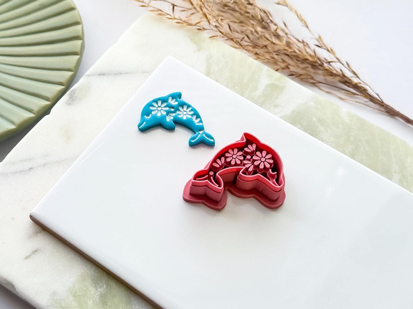 Side view of a dolphin-shaped polymer clay cutter with decorative floral embossing shown alongside a blue clay impression. UK-made crafting tool for polymer clay, fondant, jewellery making and creative craft projects.