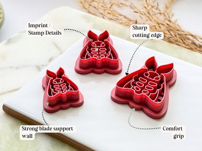 Side view of a moth-shaped polymer clay cutter in dark pink PLA, highlighting the sharp cutting edge, reinforced support wall, embossed stamp details and comfortable grip handle. Displayed on a white tile with decorative dried grasses.
