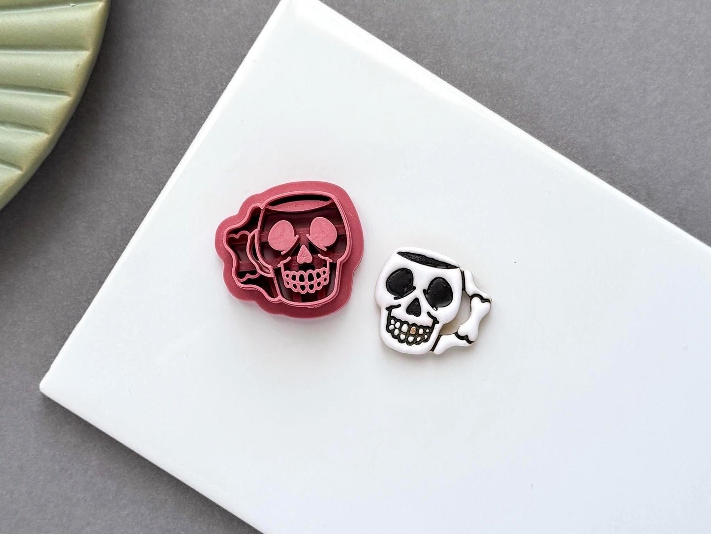 Skull mug polymer clay cutter with detailed embossed design shown next to a matching clay cut-out. UK-made clay tool for Halloween earrings, jewellery making, fondant decorating and handmade craft projects.