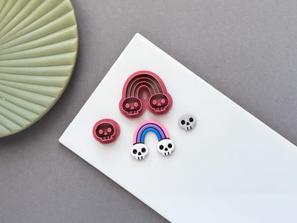 Gothic rainbow polymer clay cutter featuring skull details at each end, shown with matching clay impressions and a small skull cutter. Ideal for Halloween-themed jewellery making and fondant projects.
