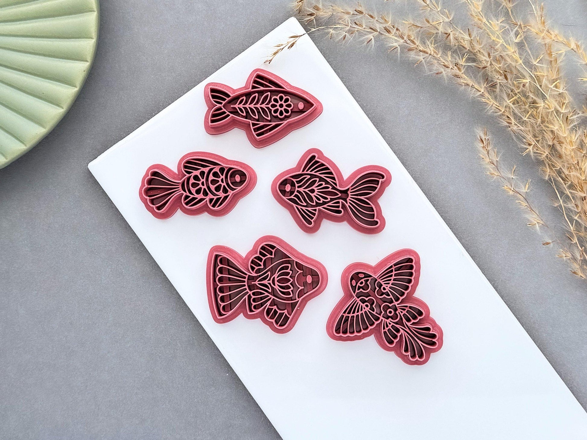 Five dark pink floral folk art fish polymer clay cutters displayed on a white tile.