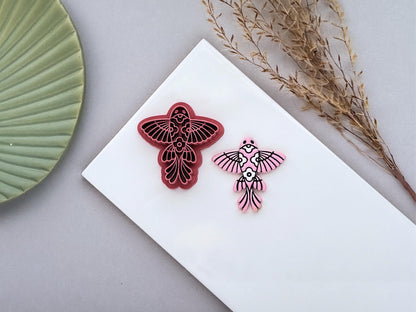 Ornamental fish polymer clay cutter displayed beside a matching pink clay cut-out. The folk art-inspired fish design features intricate fin and floral details and is photographed on a white ceramic tile.